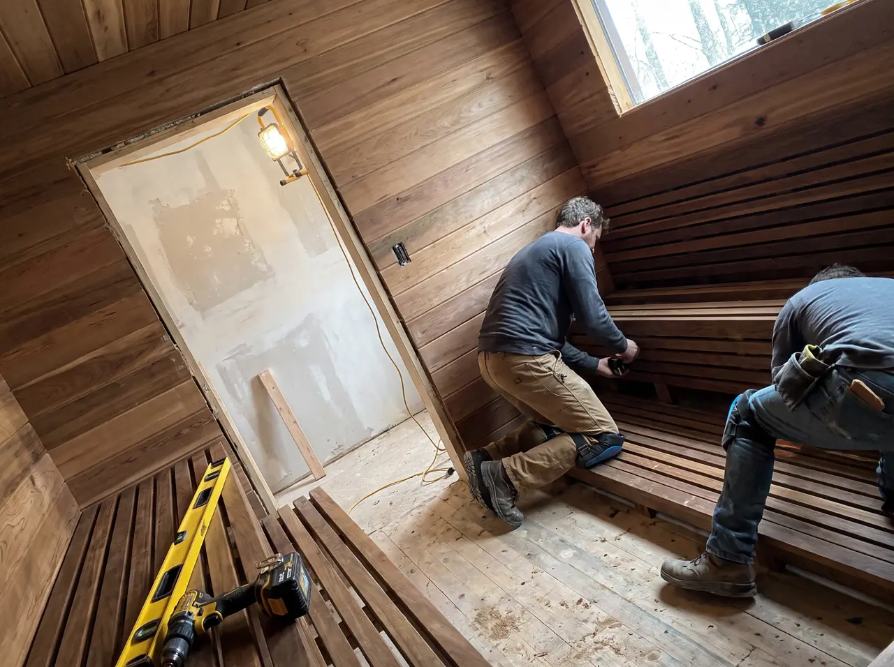 Instaladores fixando banco de cumaru dentro de sauna em obra